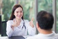 Asian professional woman doctor smiles and shows thump up sign or Ã¢â¬ÅVery goodÃ¢â¬Â with her patient due to his healthcare at